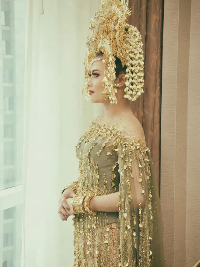 Pengantin bermahkota dan berkebaya keemasan di dekat jendela
