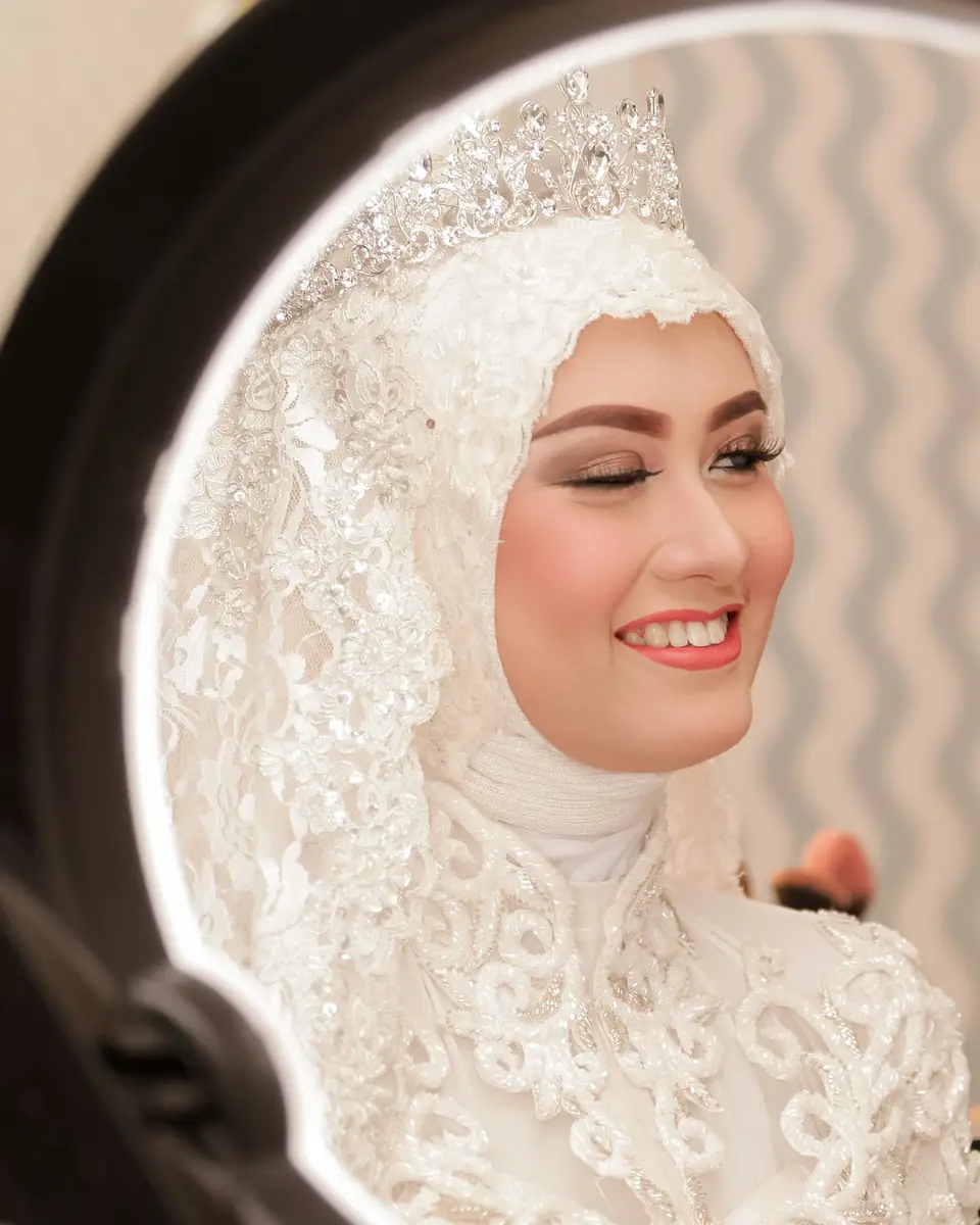 Pengantin berkerudung renda dan tiara tersenyum di depan cermin rias